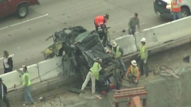 Overturned car dangles over highway median